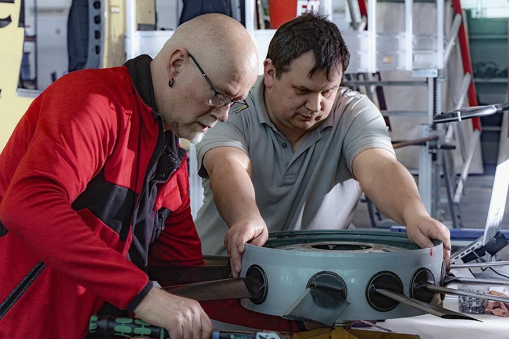 Zwei Fluggerätmechaniker arbeiten an einem ausgebauten Fenestron eines Hubschraubers.