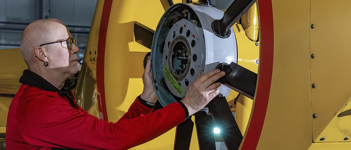 Ein Fluggerätmechaniker arbeitet an einem Fenestron eines gelben Hubschraubers.