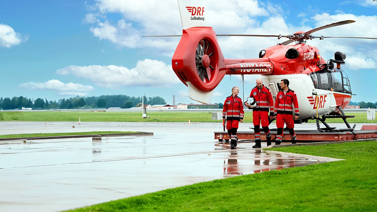 Die Crew eines Rettungshubschraubers läuft nebeneinander. Im Hintergrund ein Hubschrauber der DRF Luftrettung.